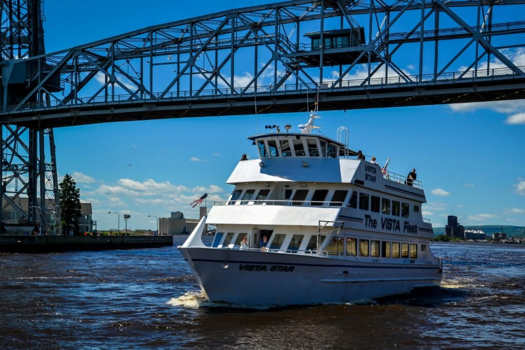 Places to Explore A Vista Fleet boat cruises under Duluth's iconic Aerial Lift Bridge on a sunny day.